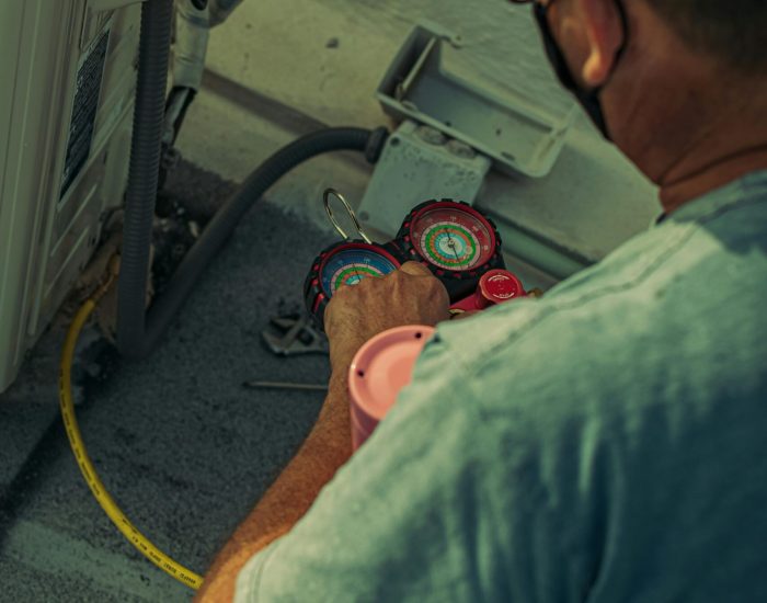 Professional technician repairing an outdoor air conditioning unit with gauges and tools.